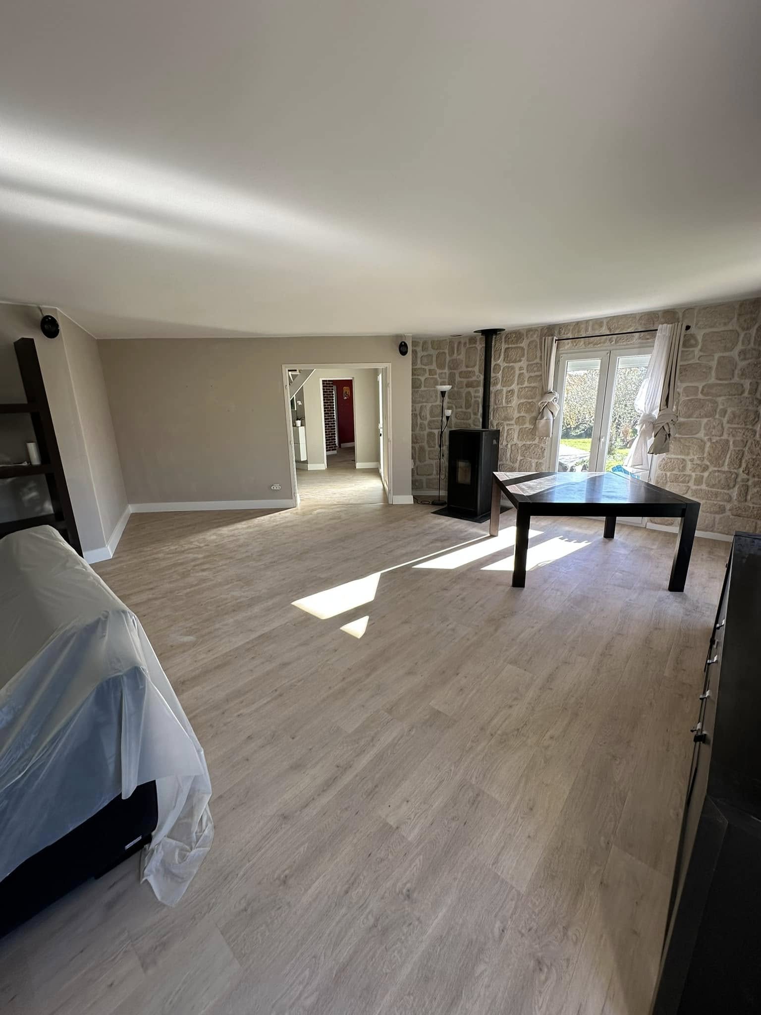 Salon lumineux moderne avec parquet posé par jordan harkat à montauban, murs en pierre beige et poêle noir cosy